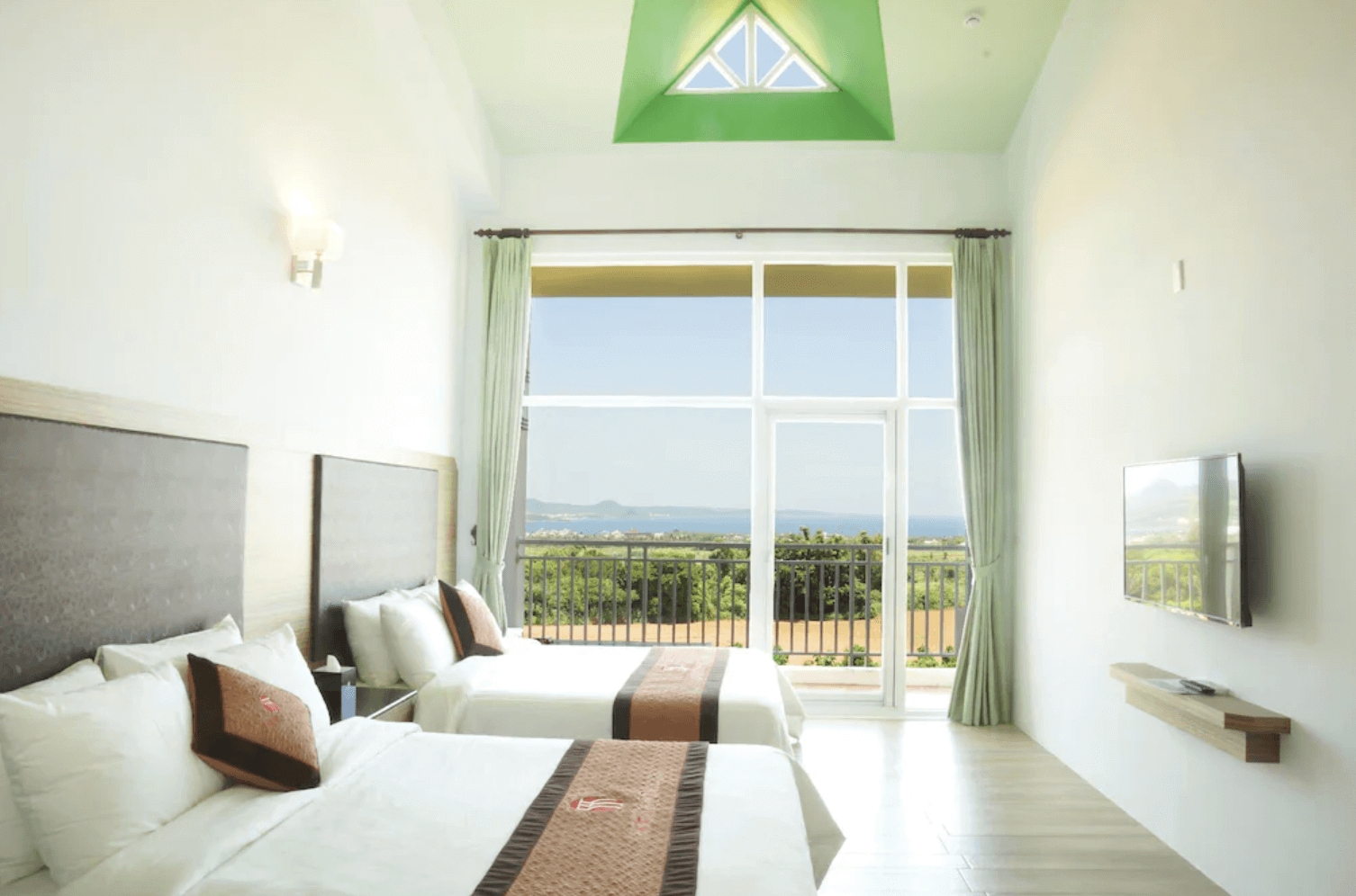 【恆春住宿】珊瑚園民宿海景四人房，挑高天花板與大面落地窗引進自然光與遠方海景，清新淡綠色窗簾與簡約設計風格，營造舒適放鬆的住宿氛圍。