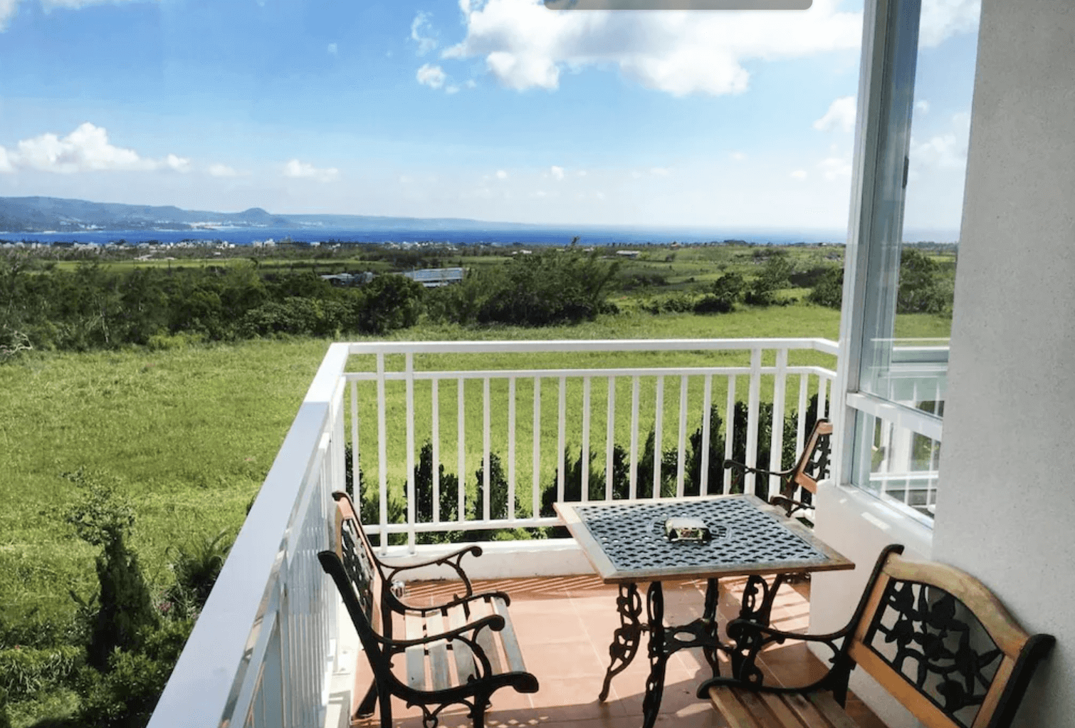 【恆春住宿】珊瑚園民宿陽台景觀區，擺放著鐵製座椅與桌子，可遠眺一望無際的綠意田野與藍天大海，適合愜意地享受戶外早晨或黃昏時光。
