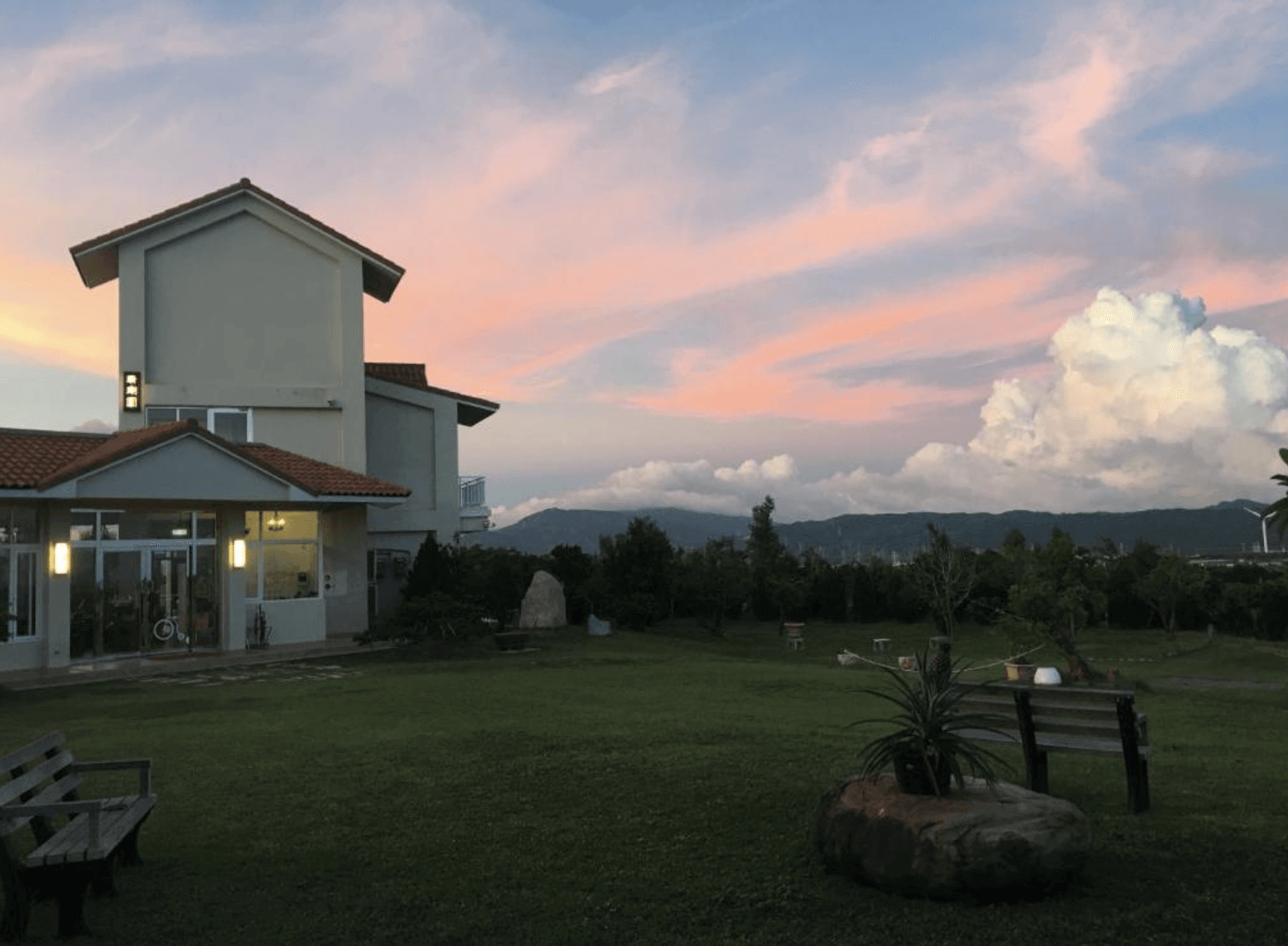 【恆春住宿】珊瑚園民宿戶外庭園與建築外觀，夕陽餘暉映照天空與草地，環境寬敞靜謐，綠意盎然，是親子與毛孩們自由奔跑的自然空間。