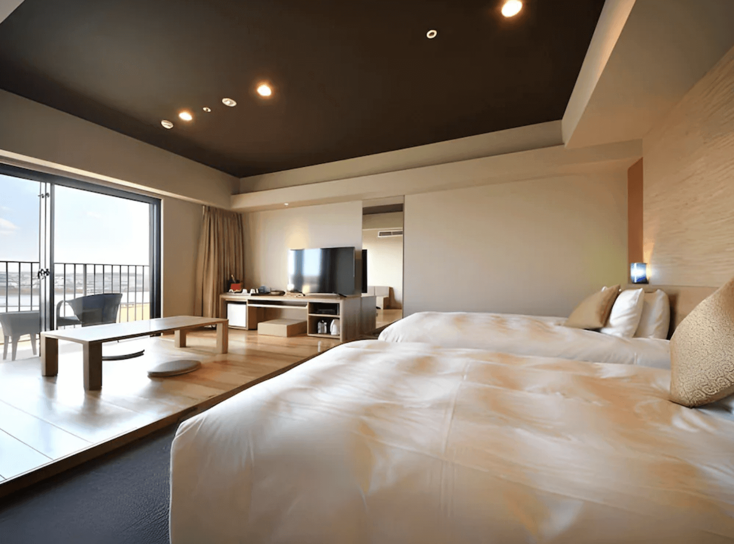 【那霸住宿】琉球溫泉瀨長島飯店和洋式客房 — 兩張雙人床與和室休憩區相連，室內可見電視、矮桌與座墊，落地窗外有陽台與海景。