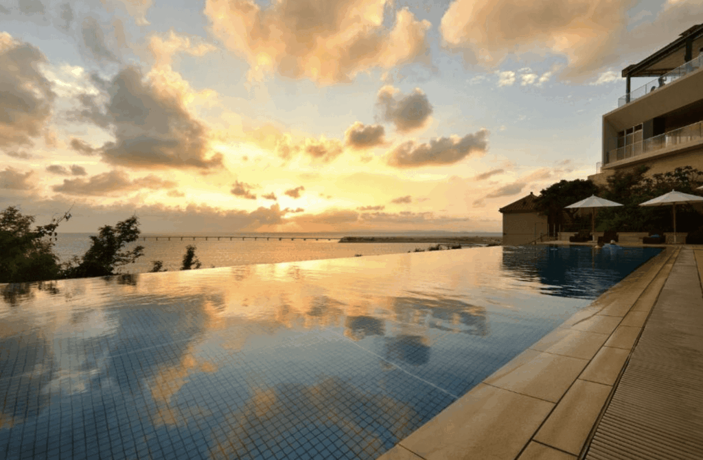 【那霸住宿】"那霸住宿精選示意圖"琉球溫泉瀨長島飯店無邊際泳池 — 夕陽映照下的泳池與大海相連，遠方可見跨海大橋與金黃色天空，充滿浪漫氛圍。