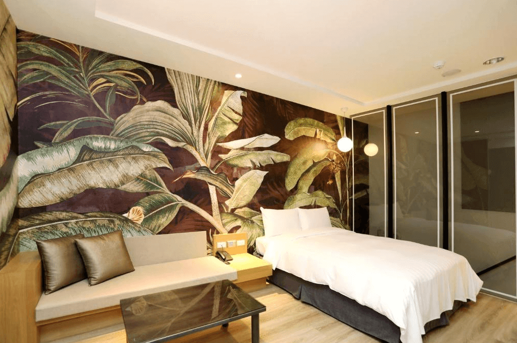 【白河住宿】"白河住宿精選示意圖"白河山籟會館房型一：設計感十足的雙人房，牆面以大型熱帶植栽壁畫裝飾，搭配現代吊燈，房內有舒適雙人床、沙發與玻璃茶几，營造出時尚又放鬆的氛圍。