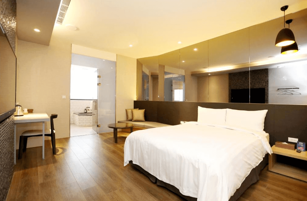 【白河住宿】白河山籟會館房型二：溫馨現代風格雙人房，木質地板搭配大面鏡面設計，空間寬敞明亮，內有雙人床、沙發、工作桌，浴室採透明玻璃隔間設計。