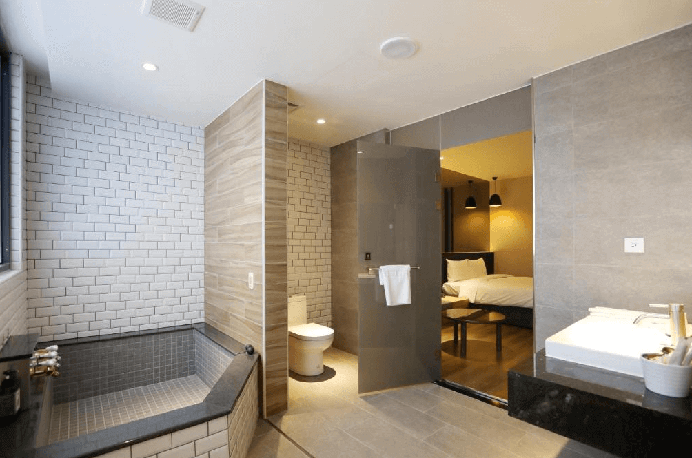 【白河住宿】白河山籟會館浴室：現代化設計的衛浴空間，設有大理石溫泉浴池、洗手台與馬桶，大片玻璃門連接臥室，整體風格高雅舒適。