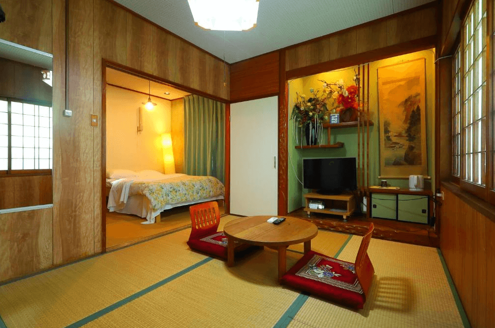 【名護住宿】白濱鄉村飯店 (Vintage Inn Shirahama Hotel) 和洋式客房，榻榻米地板搭配低矮木桌與坐墊，房間內設有雙人床與電視，營造傳統日式與現代舒適結合的氛圍。