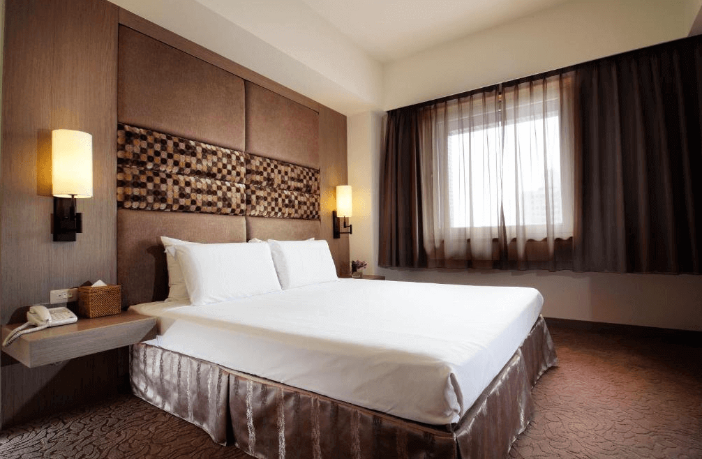 【大安住宿】福華國際文教會館客房 —— 雙人床鋪設於典雅簡約的房間內，兩側設有壁燈與木質床頭裝飾，窗邊採光明亮。