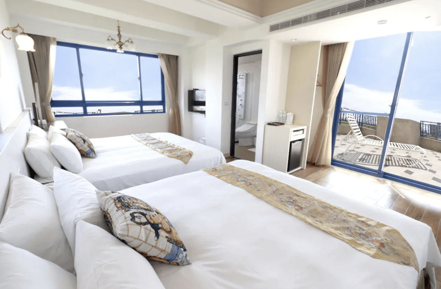 【吉安住宿】自在海民宿海景四人房，兩張大床搭配白色寢具與金色床旗，大面窗戶與陽台可欣賞藍天海景，房內設有獨立衛浴與小冰箱。