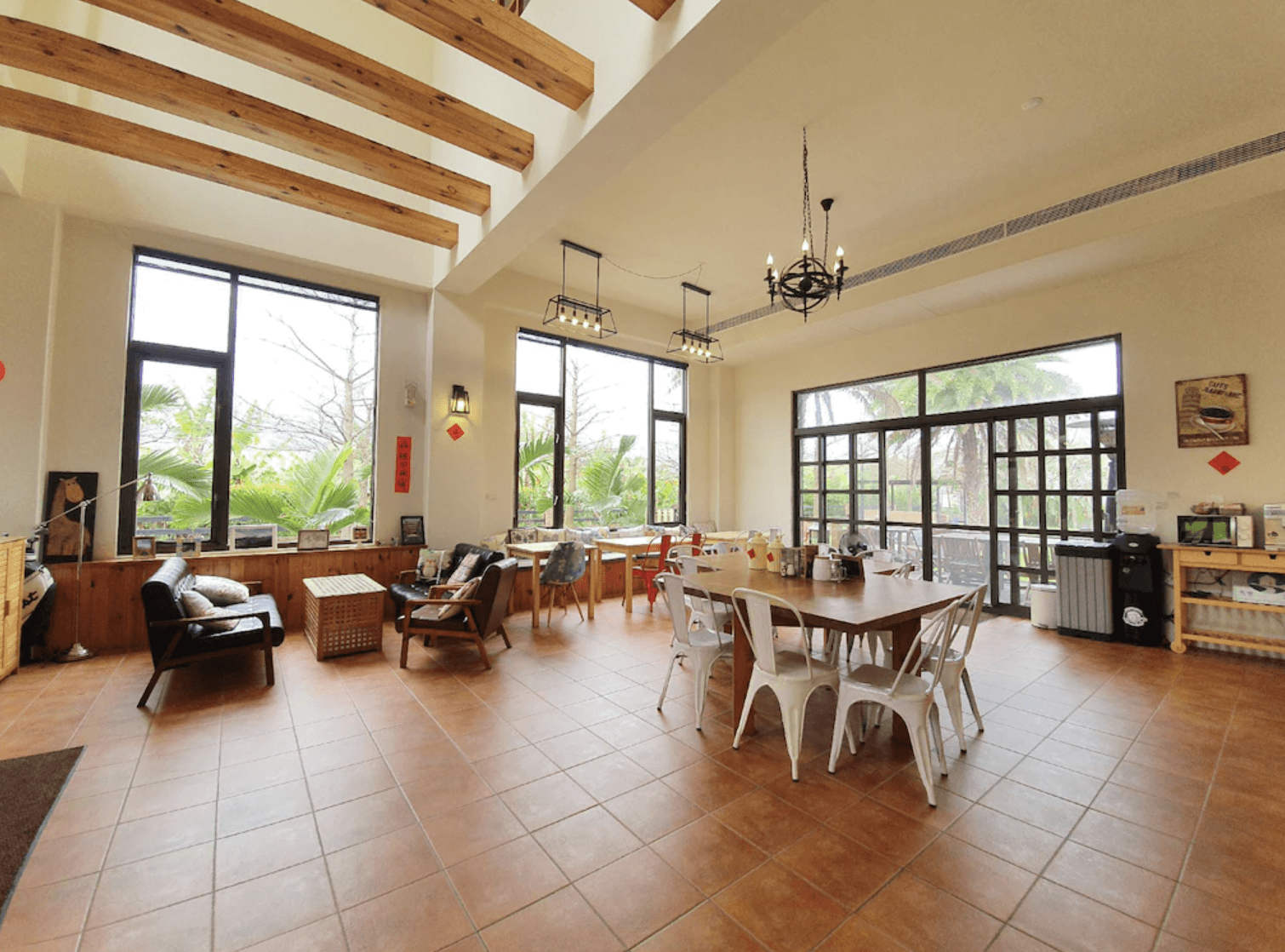 【吉安住宿】花蓮森林中民宿 公共交誼廳 — 明亮挑高空間，大片落地窗引入綠意，設有用餐區、咖啡機與休憩座椅，適合旅客放鬆交流。