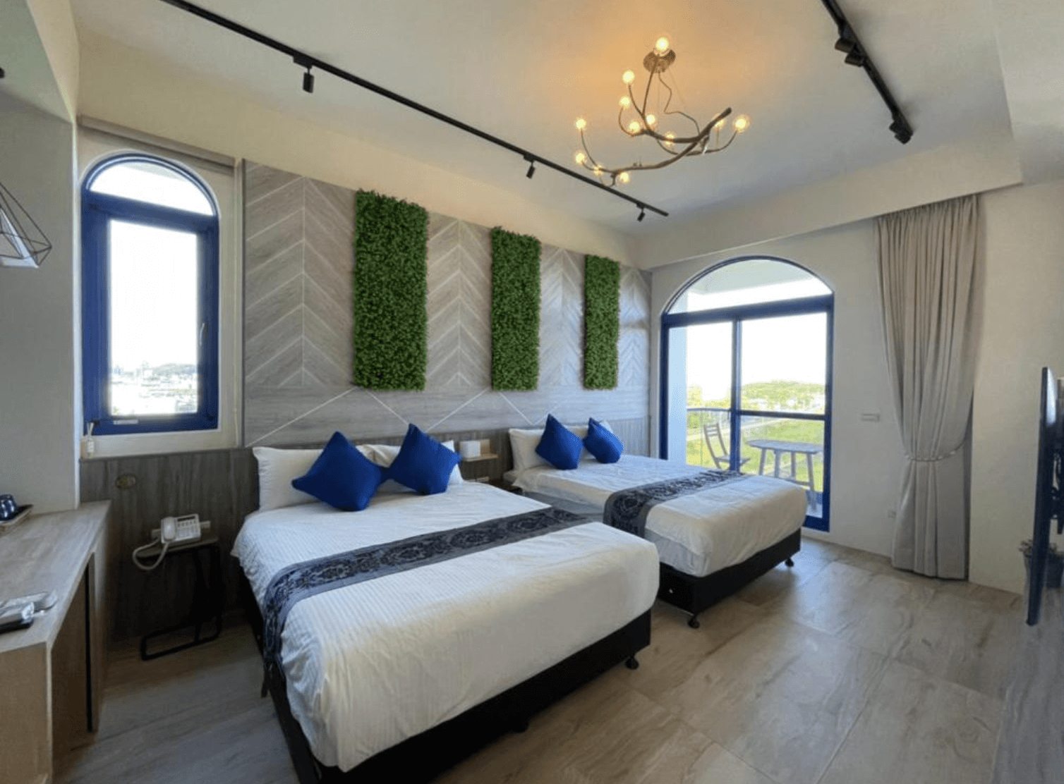 【吉安住宿】花蓮波西米亞電梯民宿 景觀雙床房 — 清新藍白色調搭配綠植牆面裝飾，設有兩張雙人床與落地窗陽台，可眺望戶外景緻。