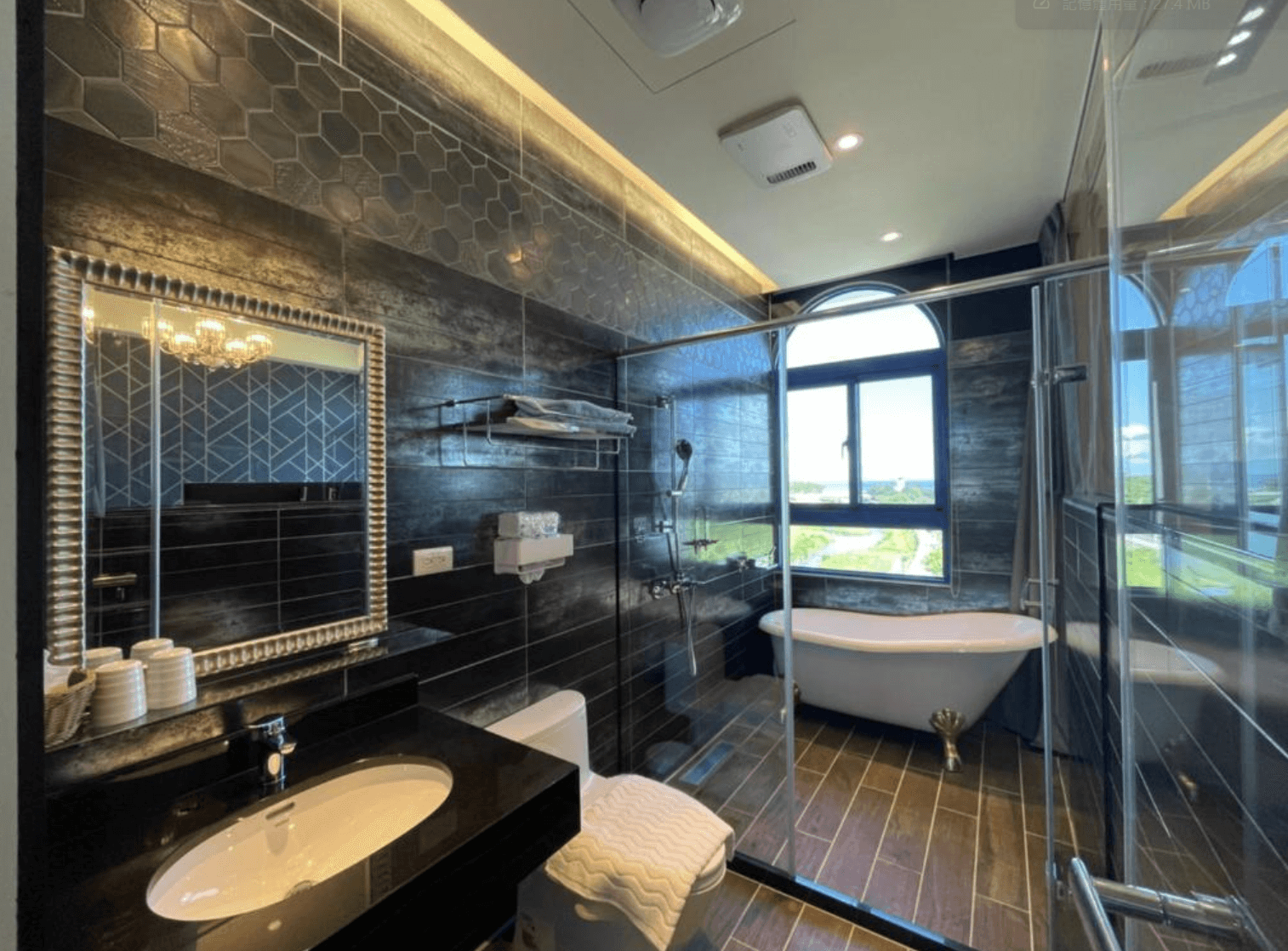 【吉安住宿】花蓮波西米亞電梯民宿 浴室空間 — 黑灰色系磁磚搭配幾何花紋，設有獨立淋浴間、復古獨立浴缸與大片觀景窗。
