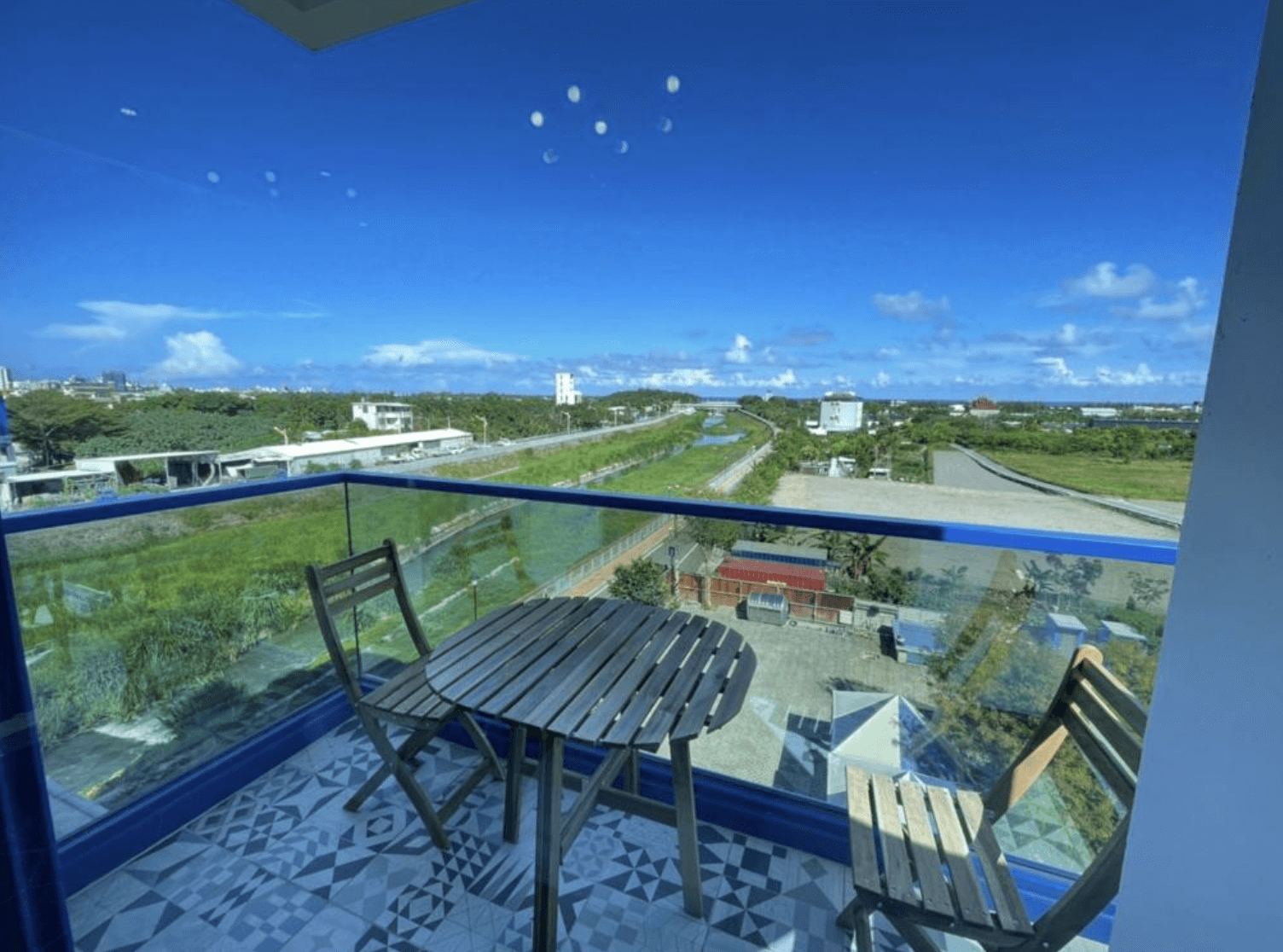 【吉安住宿】花蓮波西米亞電梯民宿 陽台景觀 — 陽台配有木質桌椅，可欣賞藍天、綠地與遠方城市景觀，享受悠閒時光。