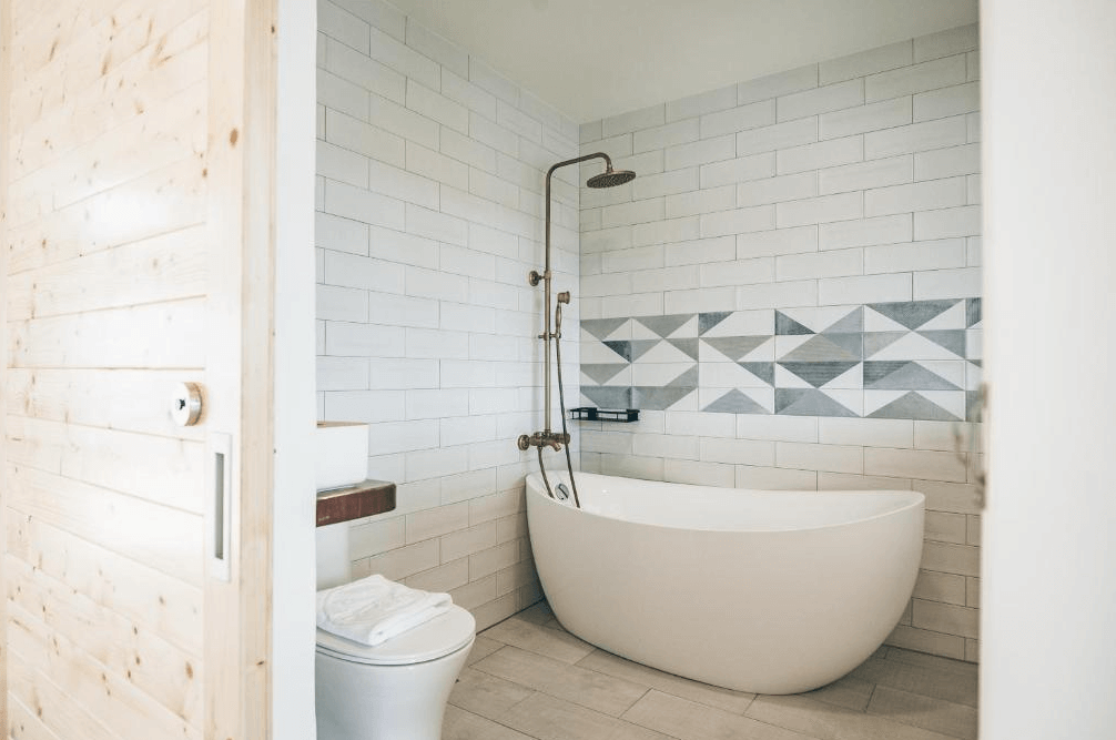 【墾丁寵物友善住宿】草分木民宿浴室 — 白色地鐵磚牆搭配幾何花磚設計，設有獨立蛋形浴缸與雨淋式蓮蓬頭，空間簡潔清新。