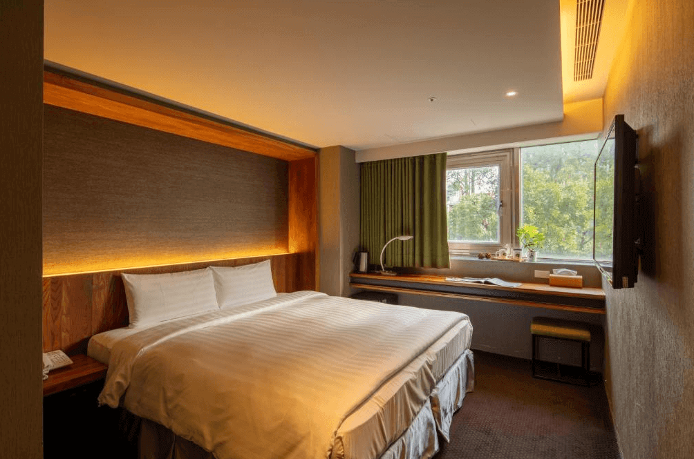 【大安住宿】谷墨商旅 GoodMore Hotel 雙人房 —— 簡約設計的大床房，床頭採用木質元素，窗邊設有書桌與綠色窗簾，光線明亮。