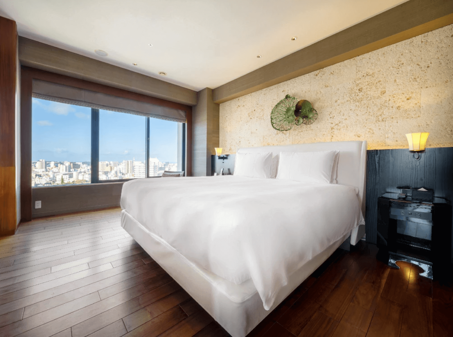 【那霸住宿】那霸凱悅酒店沖繩客房 — 現代風格的大床房，牆面以淺色石材與藝術裝飾點綴，落地窗可欣賞那霸市區景觀。