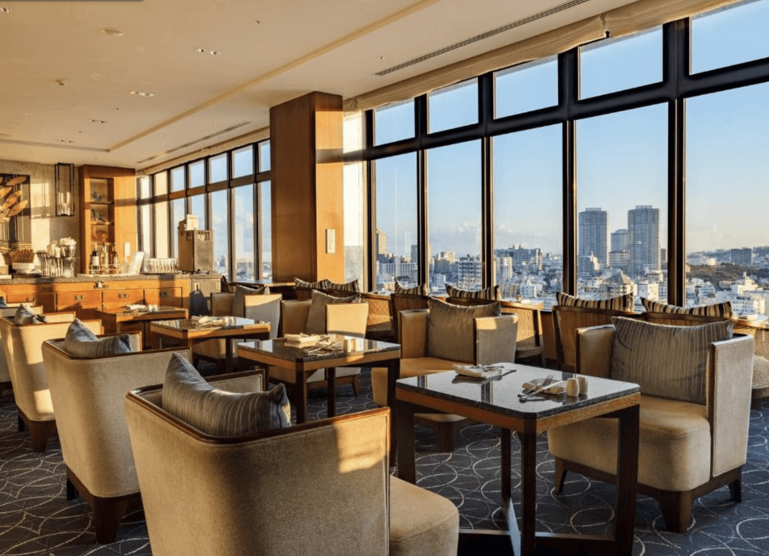 【那霸住宿】那霸凱悅酒店沖繩高樓景觀餐廳 — 寬敞明亮的用餐區，落地窗外可眺望市中心天際線，座椅舒適且氛圍高雅。