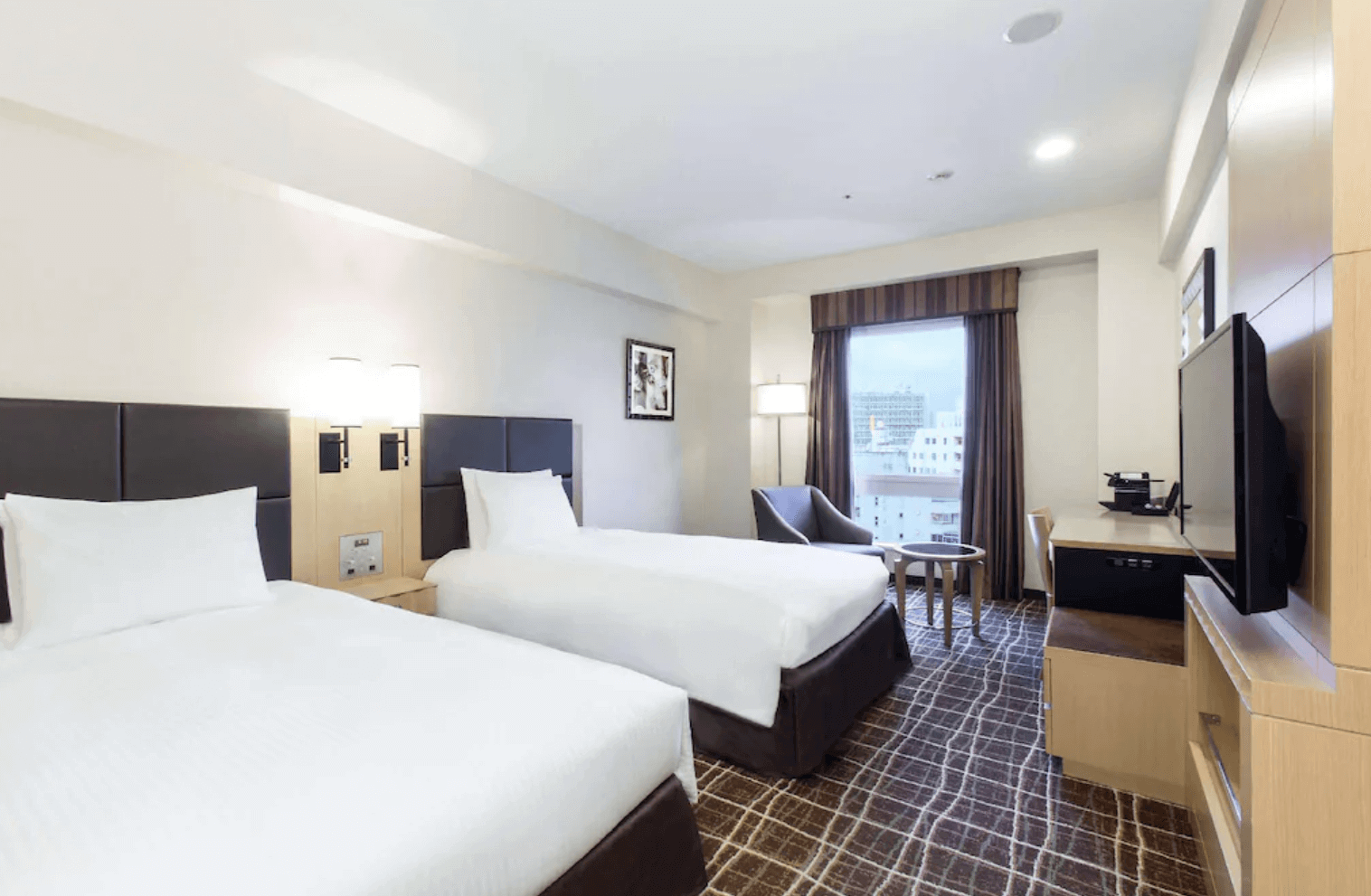 【那霸住宿】那霸希爾頓逸林飯店外觀 — 現代高層建築外觀，正面入口設有飯店招牌與迎賓車道，天空晴朗湛藍。