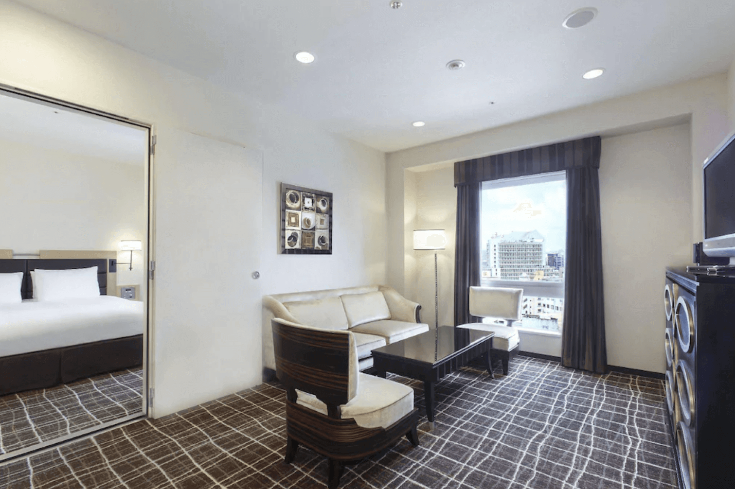 【那霸住宿】那霸希爾頓逸林飯店客房 — 兩張單人床搭配深木色家具與暖色燈光，落地窗外可見市區景觀。