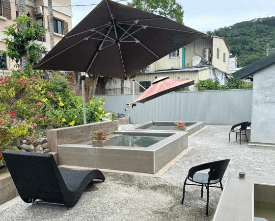 【金崙住宿】金崙有樂町溫泉民宿戶外泡湯池，配置遮陽傘與躺椅，周圍綠意點綴，提供放鬆泡湯體驗。