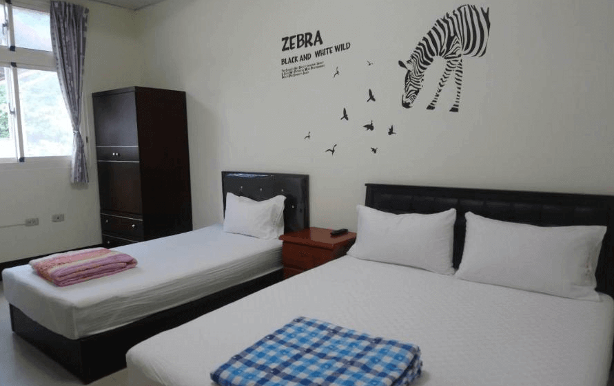 【金崙住宿】金崙鄉村民宿客房內景，設有一張雙人床與一張單人床，牆面有斑馬與飛鳥圖案裝飾，簡單整潔的住宿環境。