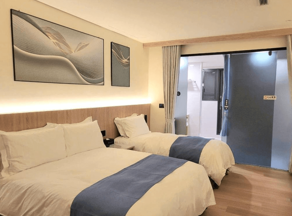 【金崙住宿】金讚溫泉飯店雙床房內景，房間內設有兩張大床，白色床單搭配藍色床尾巾，牆上有抽象藝術裝飾畫，整體設計簡約明亮。