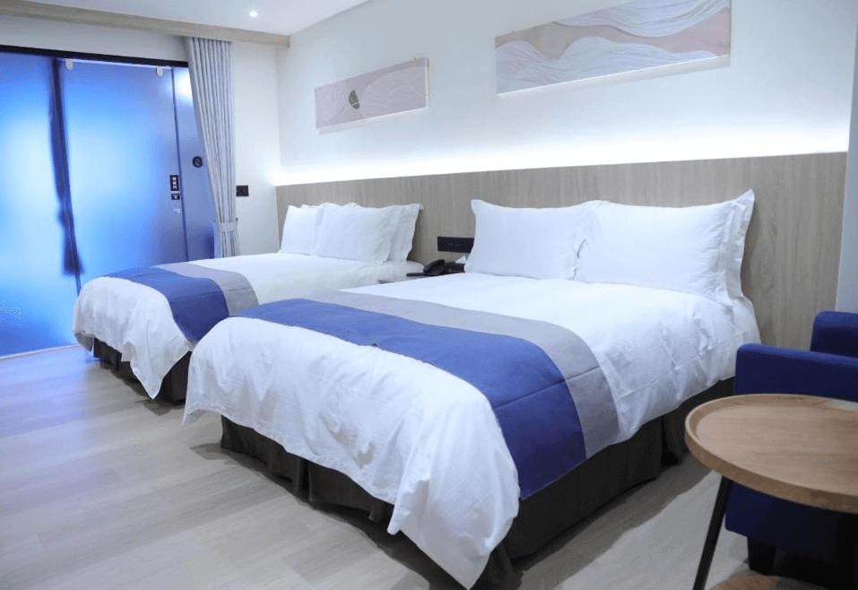 【金崙住宿】金讚溫泉飯店雙人房，兩張雙人床以藍白配色床組，背牆設計有木質感飾板與柔和燈光，整體氛圍舒適溫馨。