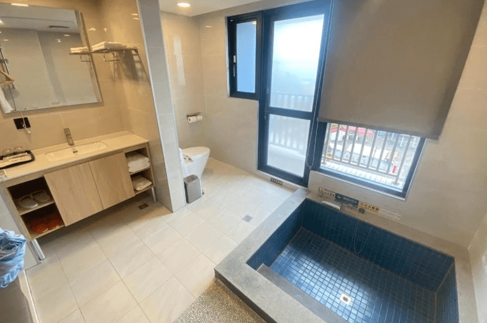 【金崙住宿】金讚溫泉飯店客房浴室空間，設有大面鏡子、洗手台與馬桶，並配置室內溫泉泡湯池，採光良好可眺望窗外景色。