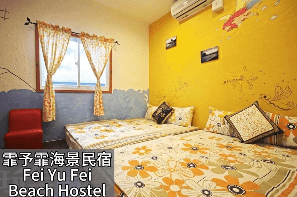 【蘭嶼住宿】霏予霏海景民宿客房一：房間以黃色與藍色海洋風格設計，牆面有飛魚與海鳥插畫，擺放兩張雙人床，床單為橘黃色花卉圖案，營造溫馨活潑氛圍。