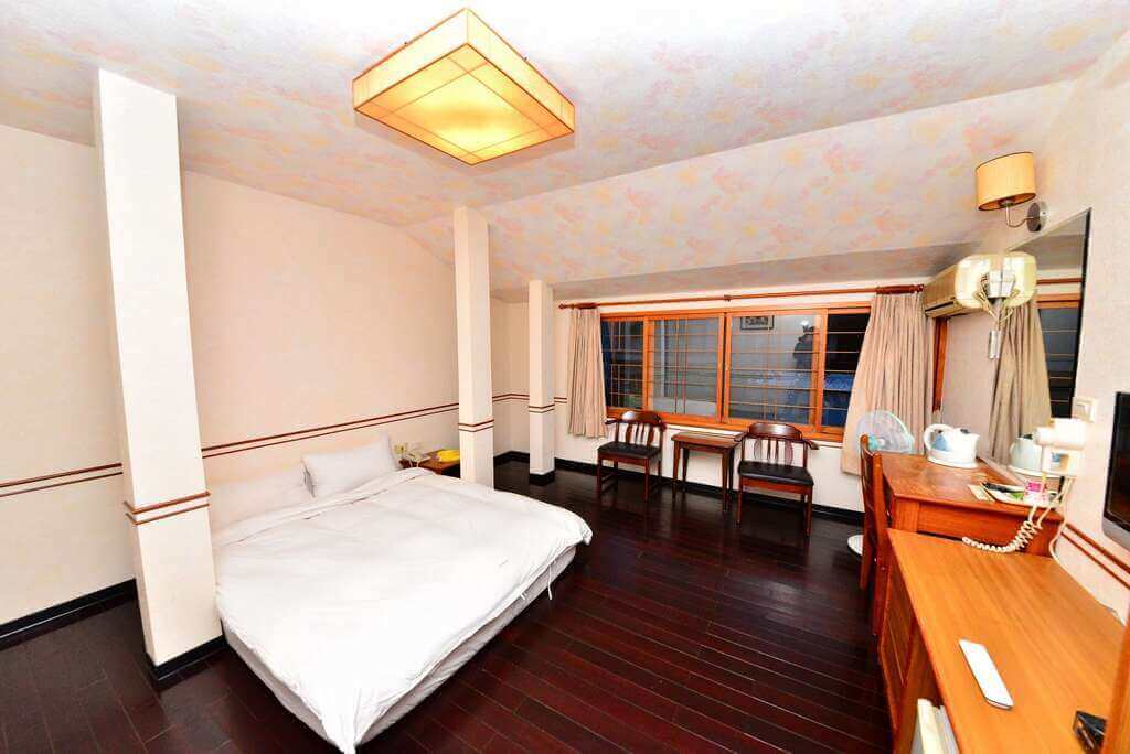 【白河住宿】靜樂館房型一：溫馨的雙人房，深色木質地板，簡潔的白色床鋪，靠窗擺放兩張木椅與小桌，房內附設書桌、熱水壺與空調。