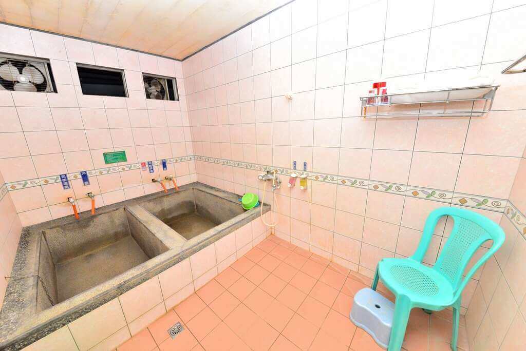 【白河住宿】靜樂館浴室二：雙人方形浴槽設計的泡湯空間，粉色磁磚搭配整齊的洗浴設施，並設有塑膠椅與小凳子，方便泡湯與沖洗。