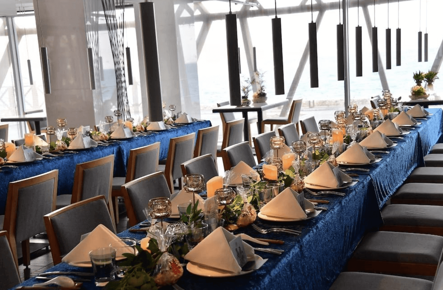 【恆春住宿】馥蘭朵墾丁 - 星沙灣海景餐廳宴會場地，長桌鋪設藍色桌巾，擺滿蠟燭與精緻擺盤，營造出浪漫典雅的用餐氣氛，窗外可見海景。