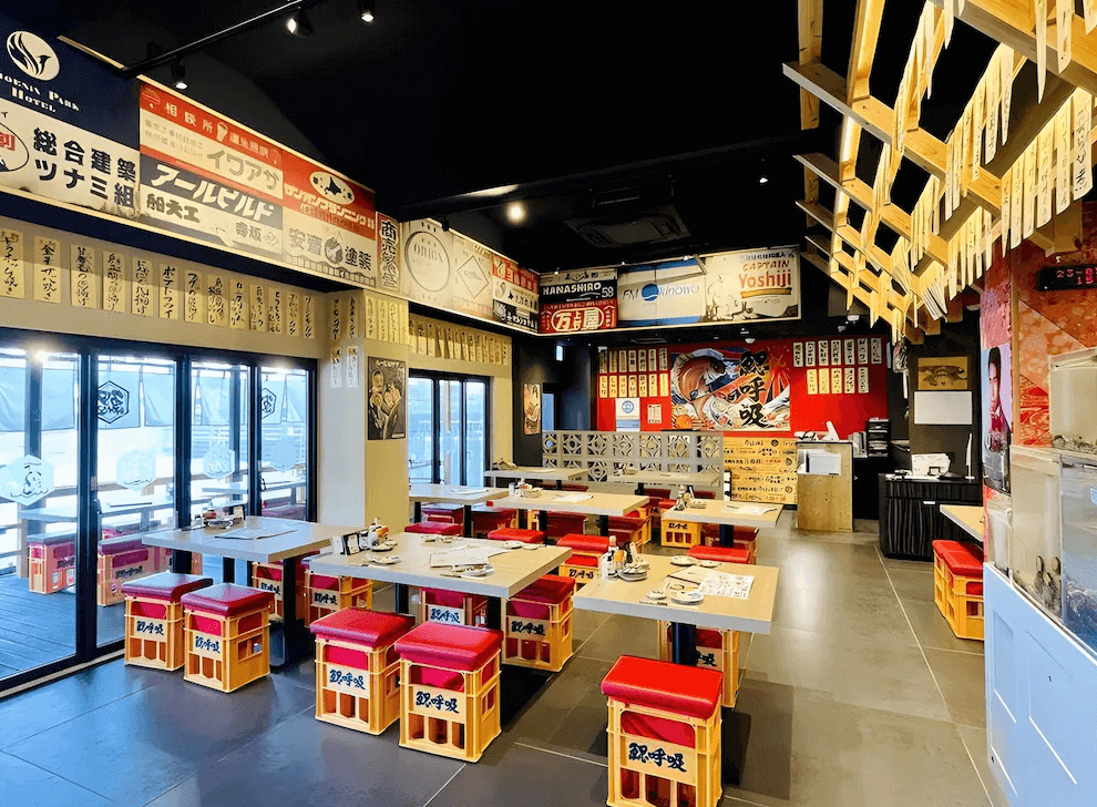 【名護住宿】鳳凰公園飯店 (Phoenix Park Hotel) 餐廳空間，充滿日式氛圍，牆上有懷舊風格的招牌裝飾，座位以木桌與紅色椅墊設計，環境熱鬧適合聚餐。