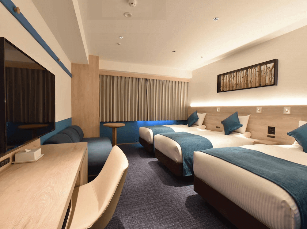 【旭川住宿】ART旭川酒店 (Art Hotel Asahikawa) 三人房，設有三張單人床，藍白色調清新現代，房內配置電視、書桌與沙發座椅，適合家庭或團體入住。