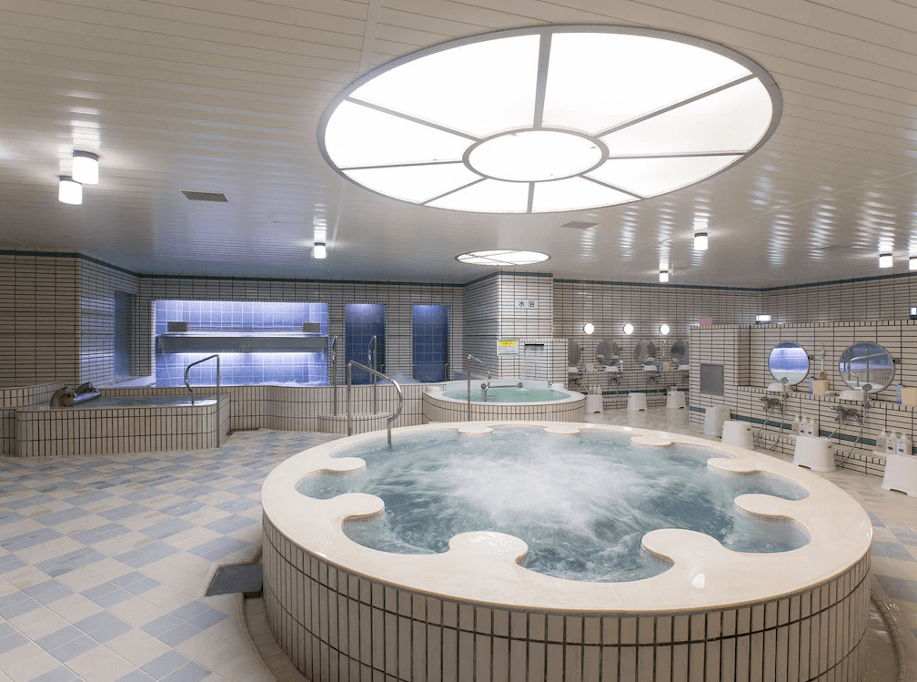 【旭川住宿】ART旭川酒店 (Art Hotel Asahikawa) 大浴場設施，圓形按摩池搭配熱水池與冷水池，明亮寬敞的空間內設有多個淋浴座位，提供舒適的泡湯體驗。