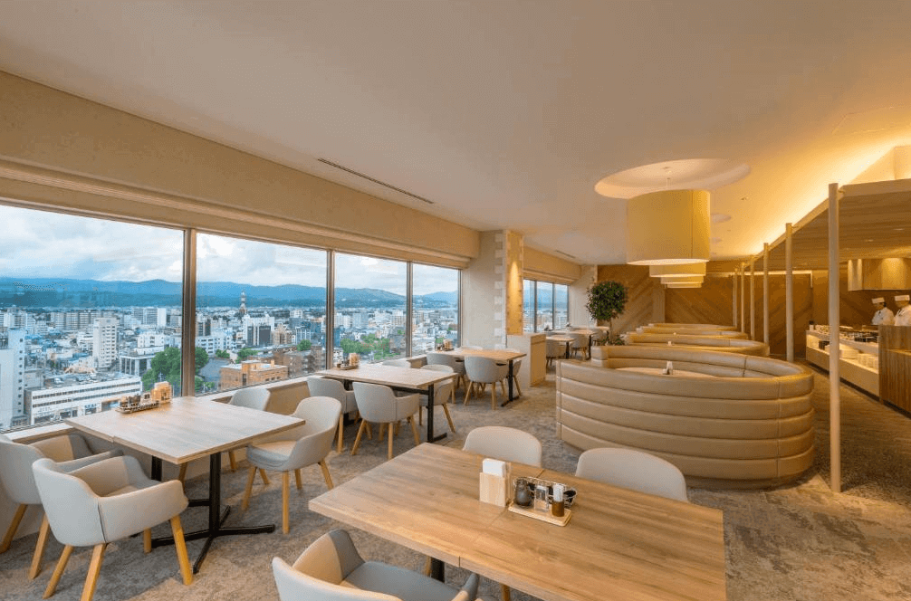 【旭川住宿】ART旭川酒店 (Art Hotel Asahikawa) 高樓層餐廳，大片落地窗可眺望旭川市區與遠方山景，木質桌椅與柔和燈光營造舒適用餐氛圍。