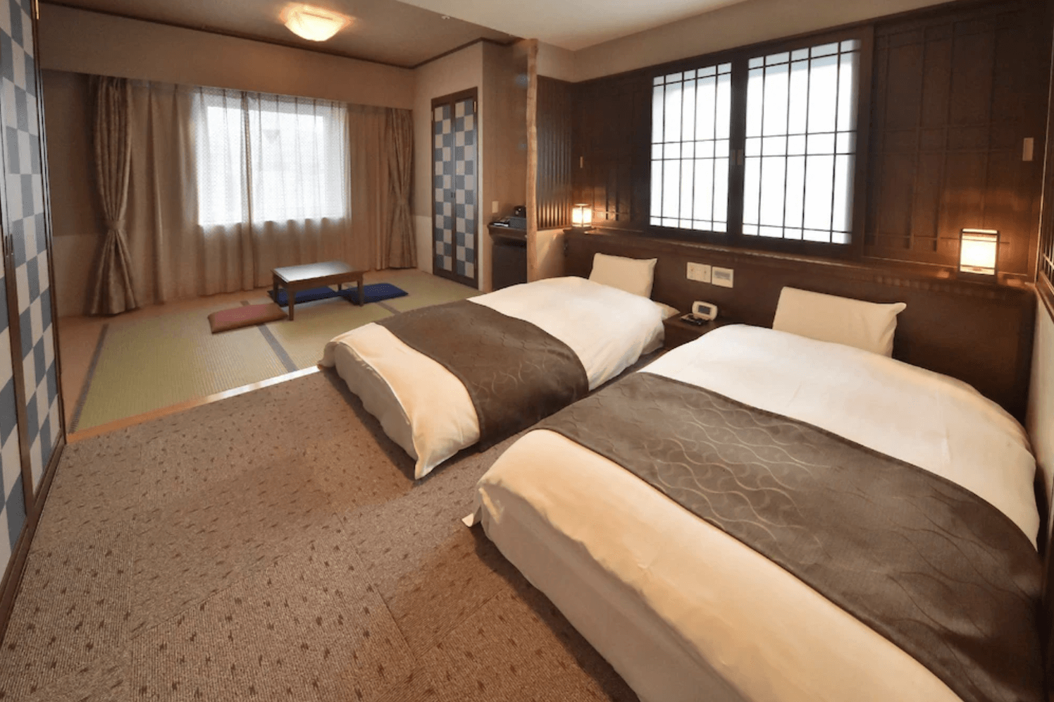 【小樽住宿】Dormy Inn小樽高級天然溫泉飯店客房，房間內設有兩張單人床，床頭有木質設計與暖色燈光，旁邊連接和式榻榻米區，擺放著低矮木桌與座墊，展現日式與現代融合的住宿氛圍