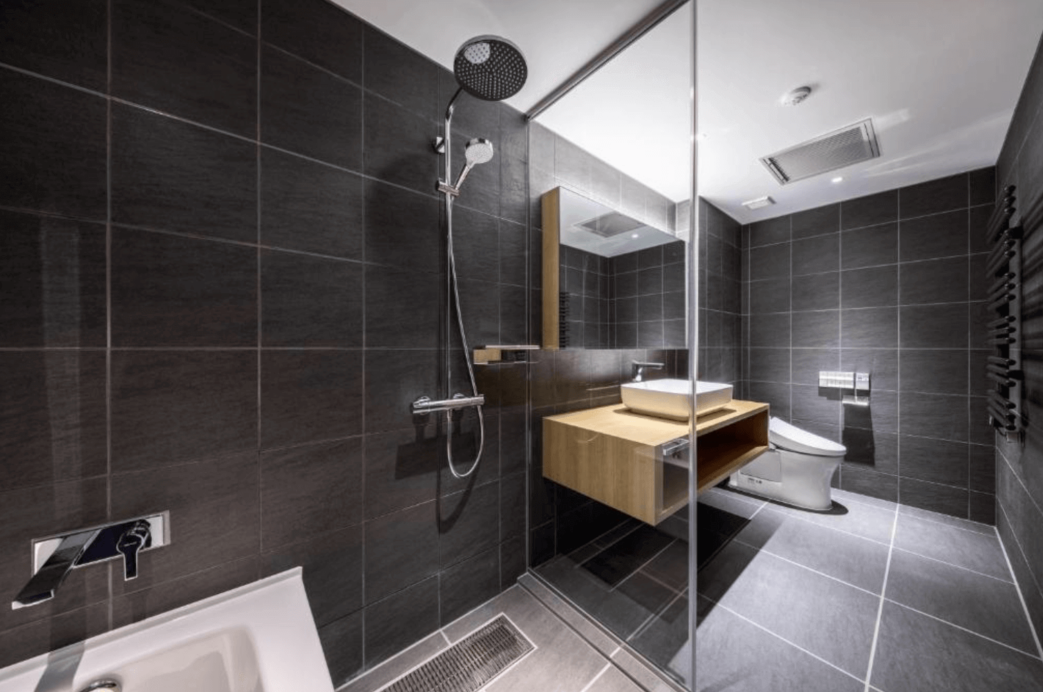 【富良野住宿】Fenix Furano飯店浴室：現代化衛浴設計，以深色磁磚搭配木質洗手台，設有淋浴間、浴缸與免治馬桶。