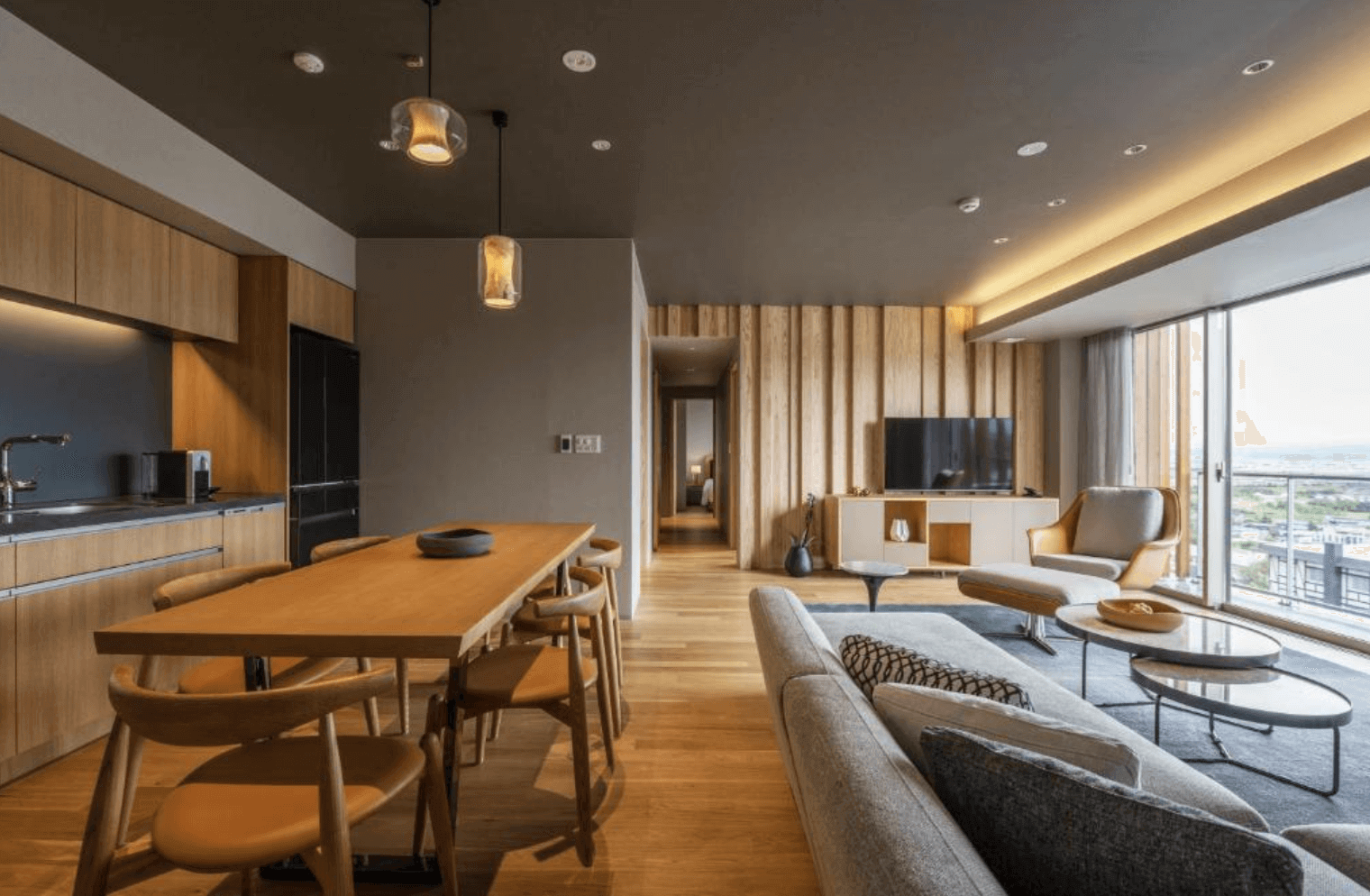 【富良野住宿】Fenix Furano飯店家庭套房公共區域：寬敞的開放式餐廳與客廳設計，木質餐桌與多張椅子，搭配沙發區與大面落地窗，能遠眺富良野美景。