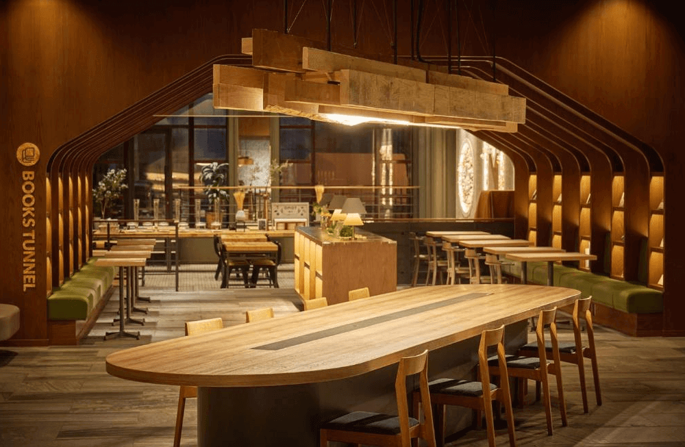 【旭川住宿】OMO7 旭川 by 星野集團大廳 Books Tunnel 公共空間，木質設計溫暖舒適，長桌與書架營造閱讀氛圍，是旅客交流與放鬆的空間。