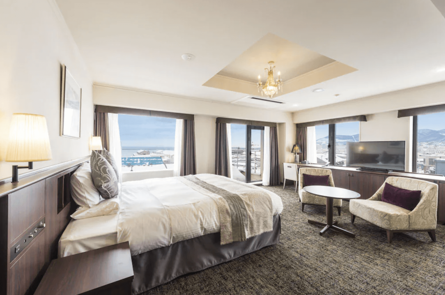 【小樽住宿】Sonia小樽酒店 (HOTEL SONIA Otaru) 豪華雙人房，設有大床、沙發椅與大面窗戶，可眺望小樽港灣與山景。