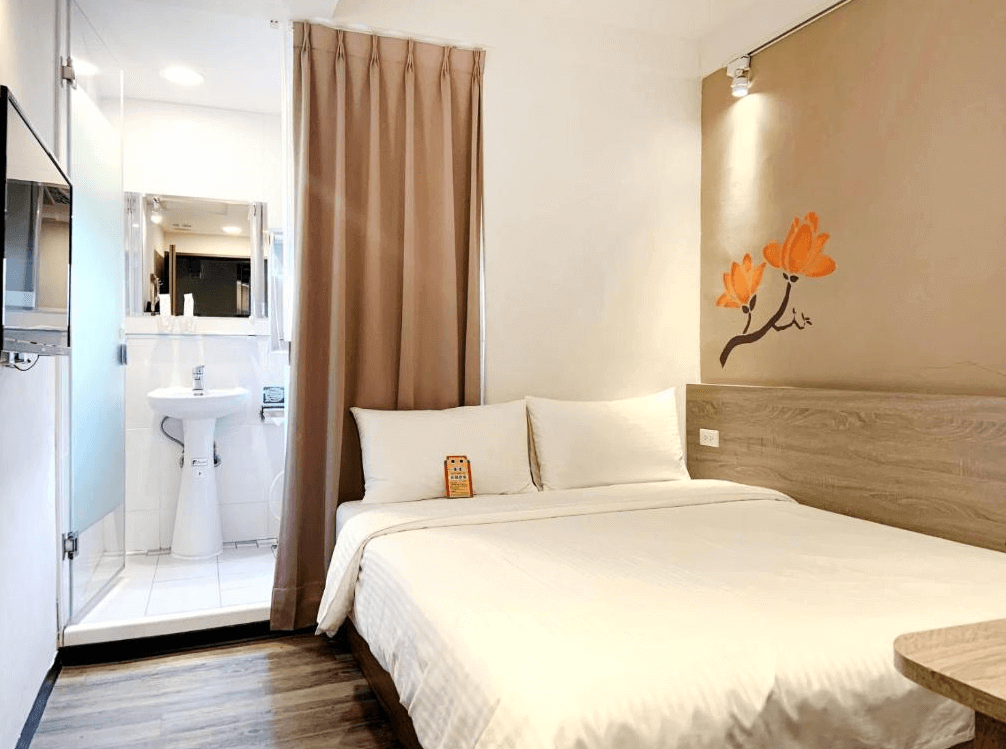 【高雄中央公園住宿】Uno青年旅舍雙人房：簡約雙人床設計，牆面有橘色花卉壁貼裝飾，附設乾濕分離衛浴與平面電視，空間溫馨明亮。