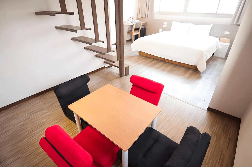 【高雄中央公園住宿】Uno青年旅舍樓中樓房型：設有雙人床與小客廳，內含四人桌椅，紅黑座椅增添活潑氛圍，空間寬敞適合多人入住。