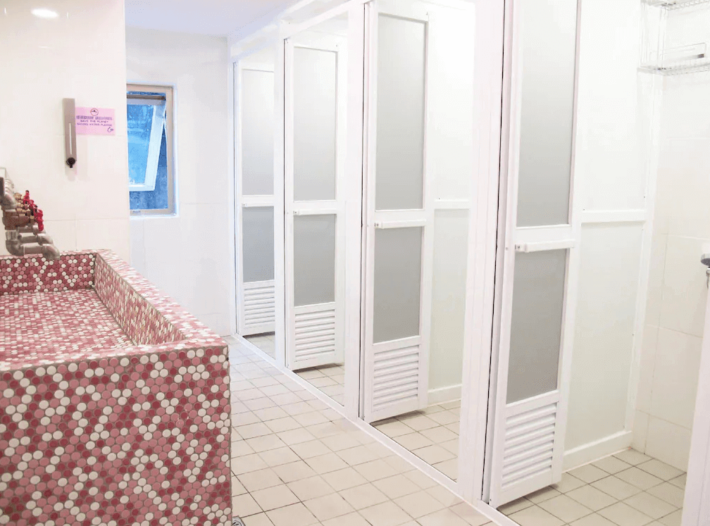 【高雄中央公園住宿】Uno青年旅舍公共浴室：明亮整潔的衛浴空間，設有多間淋浴間與粉紅馬賽克磁磚洗手檯，乾淨便利。