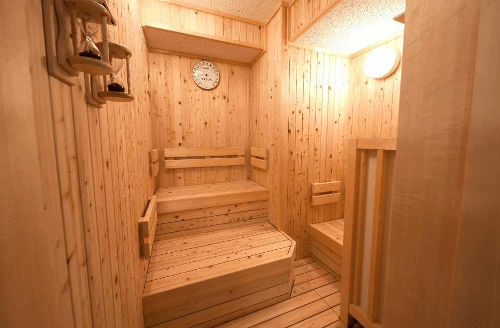 【旭川住宿】Y飯店-旭川站前 (Y's Hotel Asahikawa) 木質桑拿室，設有階梯式座位與沙漏計時器，燈光柔和，適合放鬆身心。
