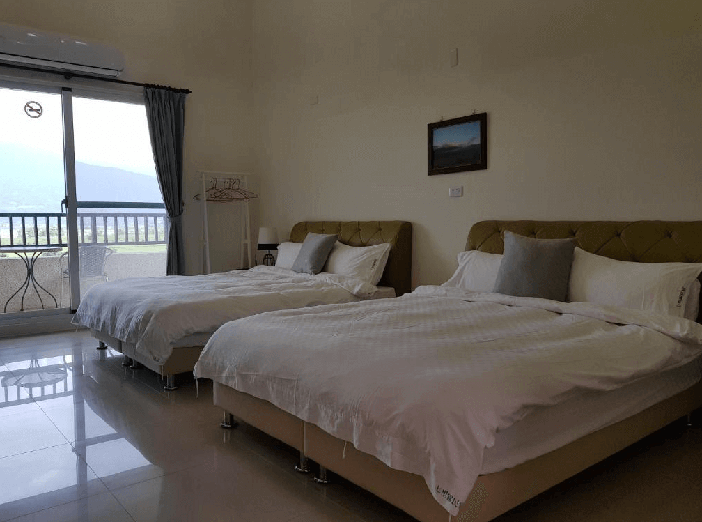 【赤柯山住宿】七里霧民宿房型二：寬敞的四人房，兩張雙人床搭配柔和燈光，落地窗旁連接陽台，窗外可欣賞遼闊綠意景觀。