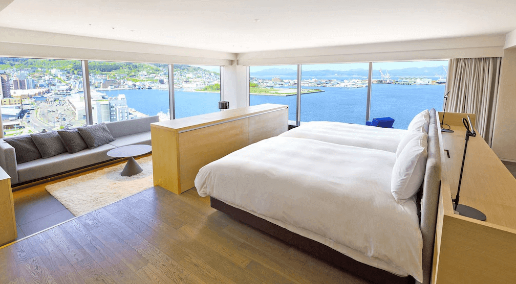 【函館住宿】"函館住宿精選示意圖"函館世紀濱海飯店高樓層海景雙床房，落地窗可一覽函館港灣與市景，房內設有舒適沙發區與木質簡約設計。
