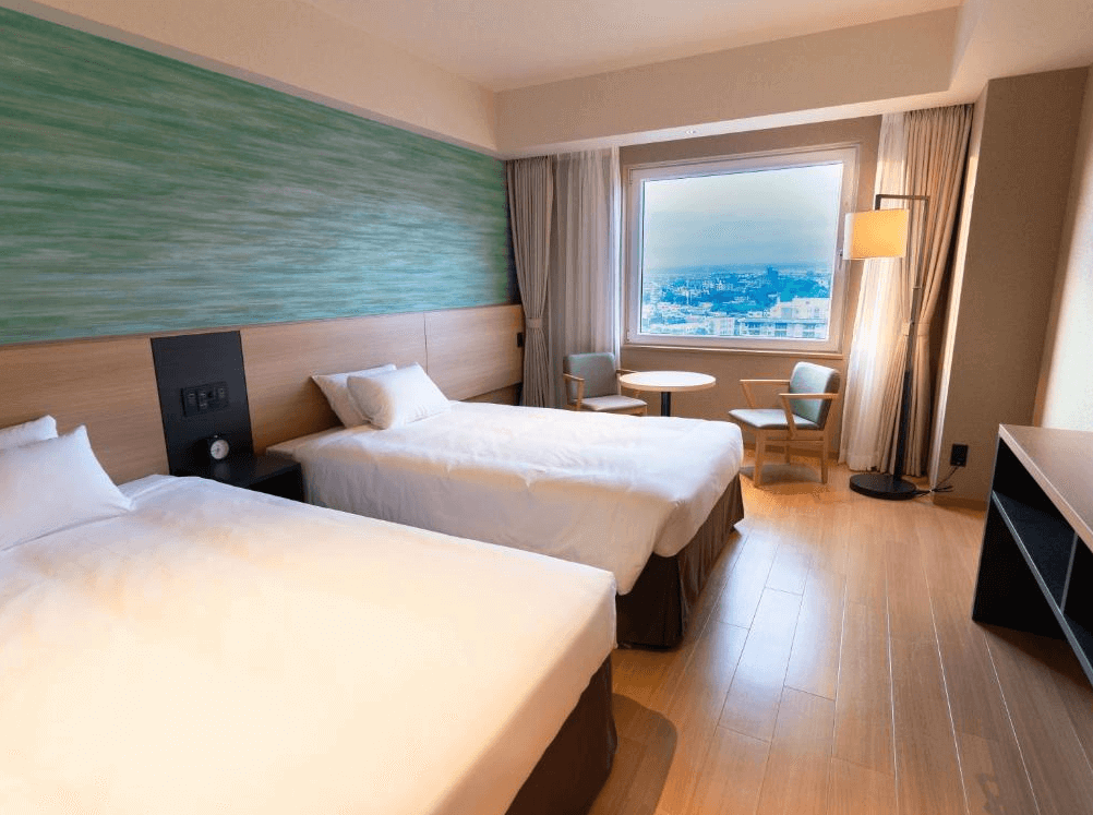 【函館住宿】函館湯之川溫泉海與燈休伊特度假村現代化雙床客房，大片窗戶可遠眺城市景觀，室內以木質地板與清新設計營造舒適氛圍。