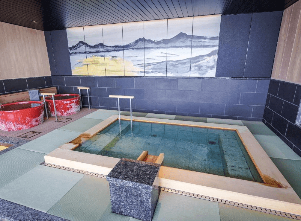 【函館住宿】函館湯之川溫泉海與燈休伊特度假村的日式室內溫泉浴場，設有木製浴池與特色紅桶湯池，牆上掛有山水畫增添和風氛圍。