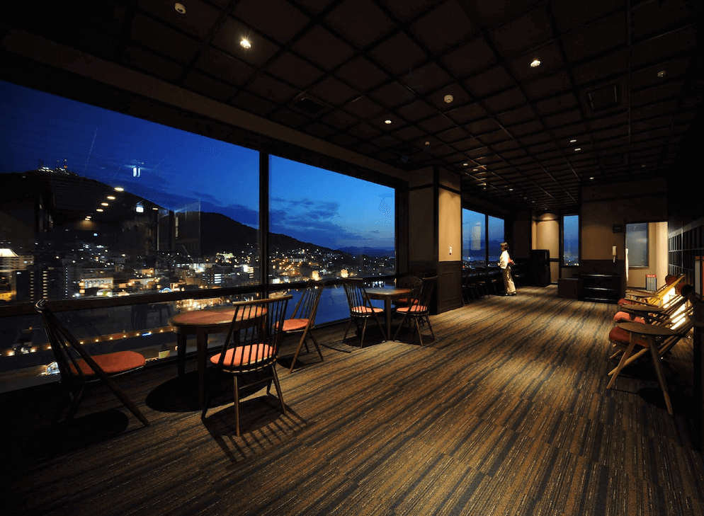 【函館住宿】函館灣 La Vista 飯店高樓層觀景休憩區，大片玻璃窗可眺望函館夜景，設有座椅與桌子，提供旅客悠閒放鬆的空間。