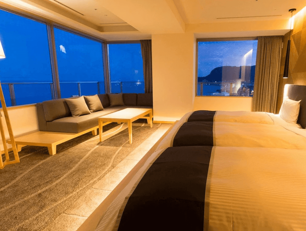 【函館住宿】函館環球景觀飯店海景雙床房，大片落地窗可欣賞函館港灣夜景，房內設有舒適沙發與木質桌椅，空間寬敞明亮。