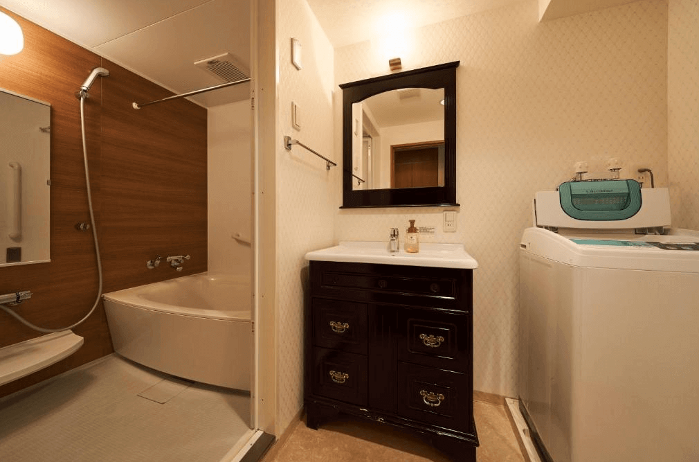 【函館住宿】函館環球景觀飯店客房浴室，設有乾濕分離淋浴間、浴缸與洗衣機，搭配復古風格洗手台，設備齊全方便長住旅客。